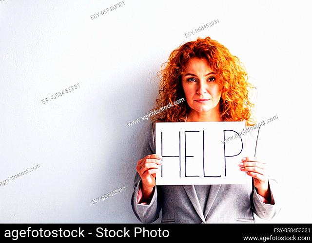 Portrait of red haired woman with the board HELP. Woman on white background showing unhappy emotions. Toned concept