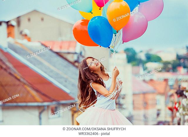 Pretty girl with big colorful latex balloons posing in the street of an old town