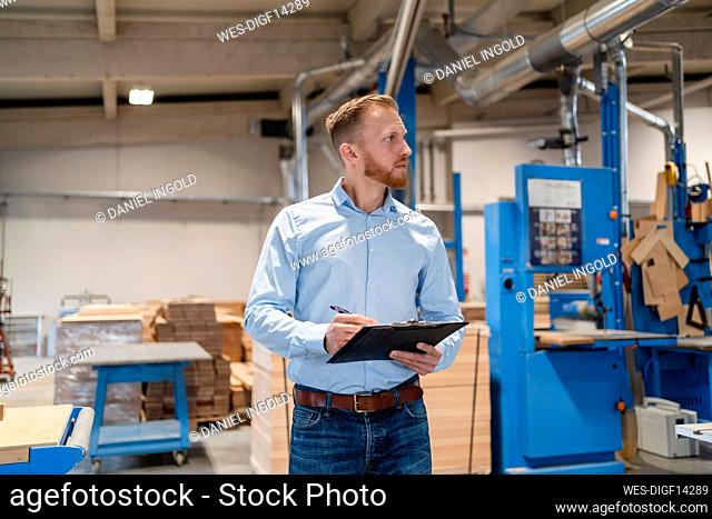 Portrait of carpenter standing in production hall with clipboard in hands