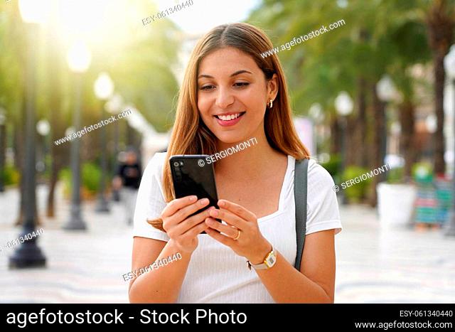 Close up of excited young woman watching her smartphone when walking in the street. Millennial girl using mobile app outdoors