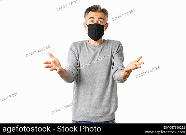 Covid-19, pandemic and social distancing concept. Portrait of startled middle-aged man in black medical mask, reaching hands forward and asking why