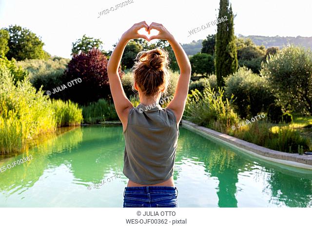 Rear view of a girl standing at swimming pool, forming a heart with her hands