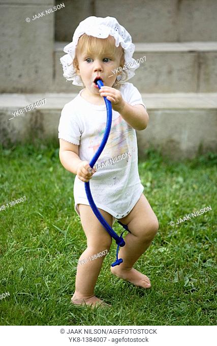 One Year Old Baby Girl Standing Outside and Blowing into Tube
