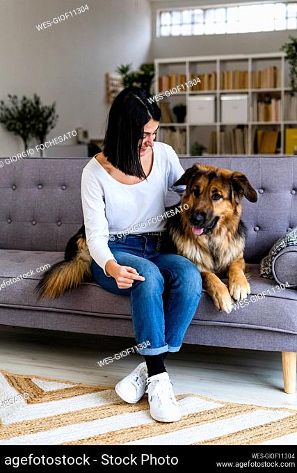 Woman with German shepherd sitting on sofa at home