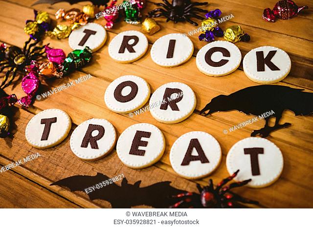 Cookies with trick or treat text by decorations and chocolates on table