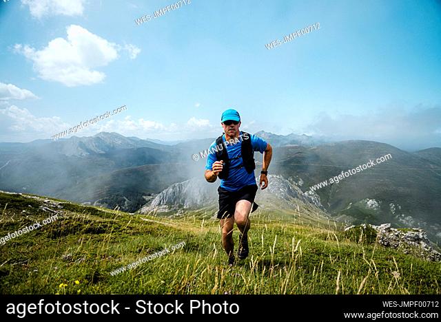 Mature sportsman trail running in the mountains on meadow against blue sky