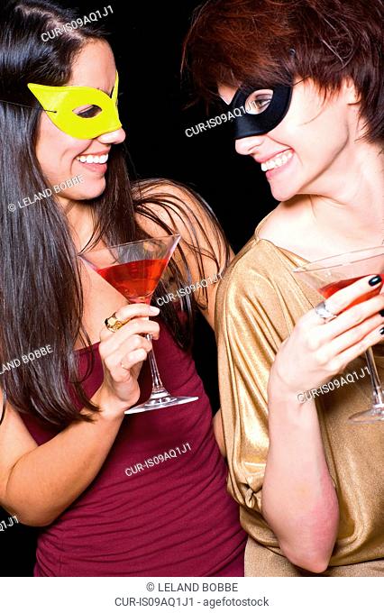 Two women wearing eye masks and drinking cocktails