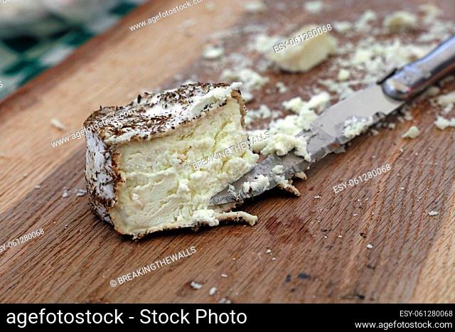 Close up one cut fresh French artisan gourmet goat cheese with herb spices and knife on wooden cutting board, high angle view