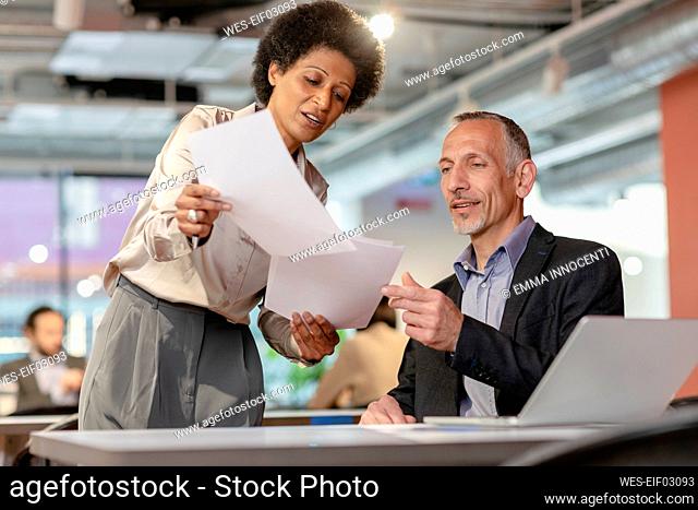 Businessman discussing with colleague over documents in coworking space