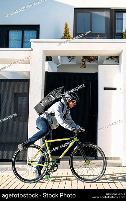 Delivery man riding bicycle on footpath by house