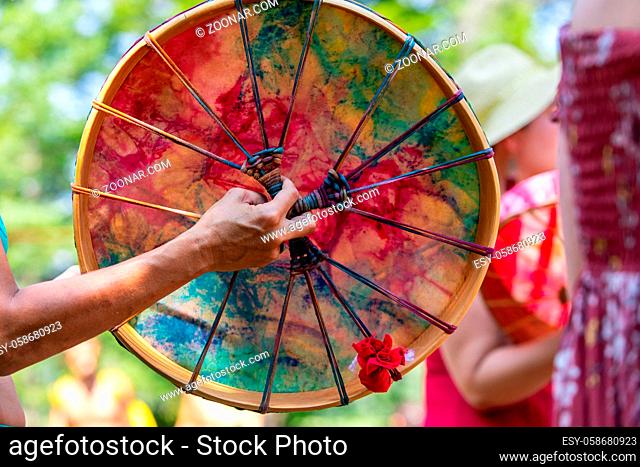selective focus on caucasian women hand playing Sacred drum, close up on colourful Native American leather drum during a music celebration in a park