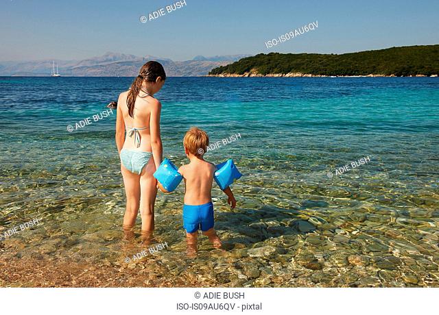 Rear view of girl and boy wearing blue armbands paddling in sea, Corfu, Greece
