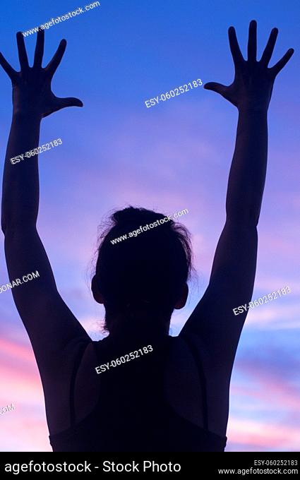 Young woman reaching for sunset sky with arms and hands outstretched in silhouette in Caceres Spain on hot summer evening