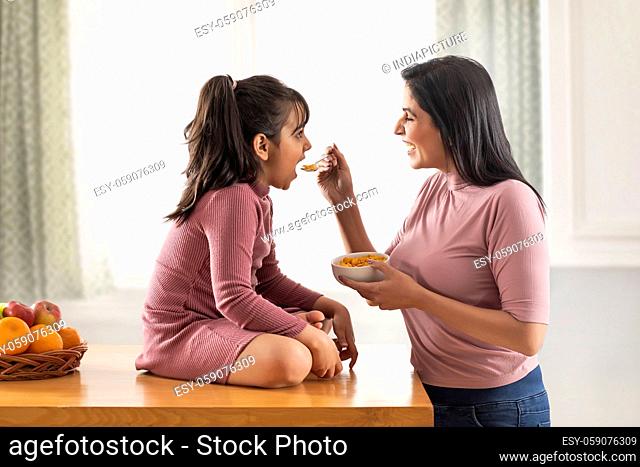 A DAUGHTER HAPPILY EATING CORNFLAKES GIVEN BY MOTHER