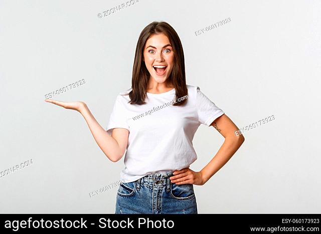 Excited beautiful girl extend arm, holding something on hand and looking happy