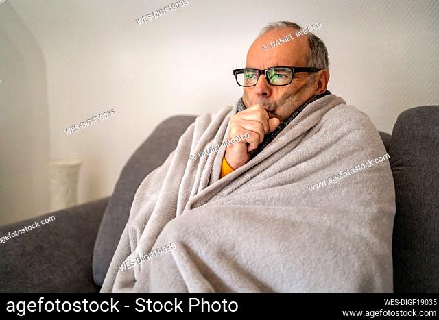 Man wrapped in blanket shivering at home