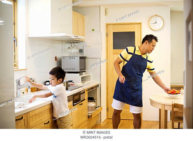 Family home. A man in a blue apron preparing a meal with his son