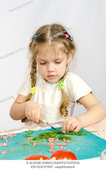 Little six year old girl intently trying to cut with a knife green kitchen table