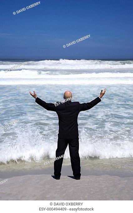 Business man standing on edge of sea arms outstretched back view