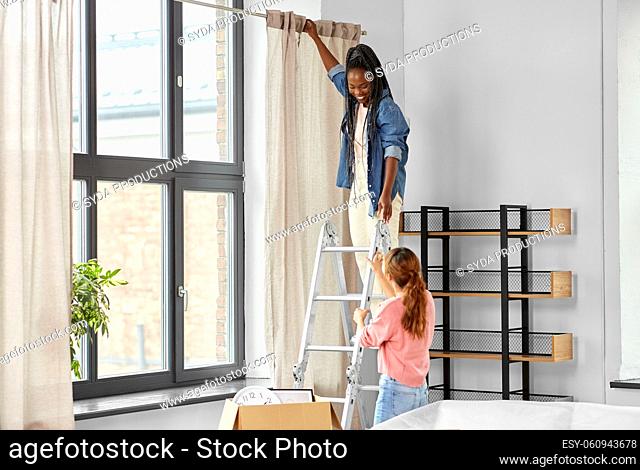 woman on ladder hanging curtains at home