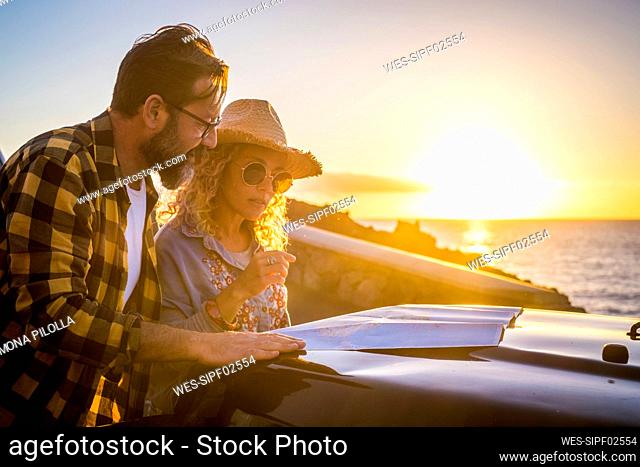 Mature couple reading map at car during sunset