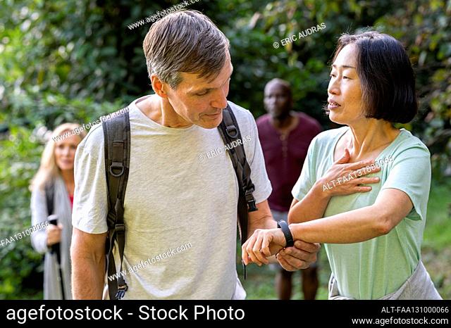 Diverse middle-aged couple taking a walk in the woods and checking lady's Fitbit device
