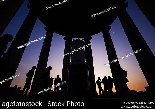 dpatop - 18 September 2020, Bavaria, Munich: Visitors to the English Garden enjoy the evening atmosphere at the ""Monopteros"" as the sun sets