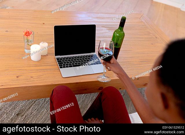 African american woman sitting on couch making video call holding glass of wine