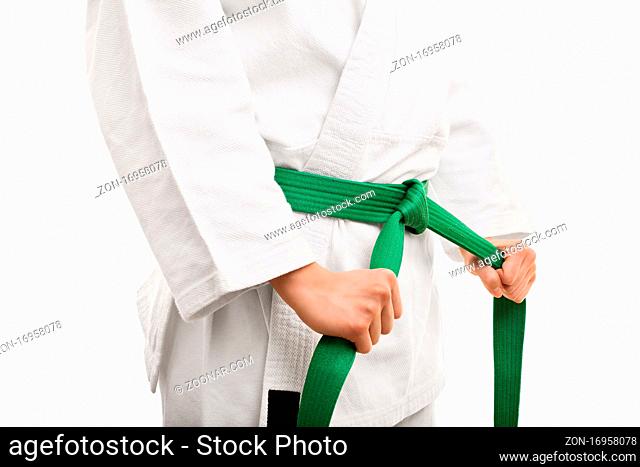 Preparing for training. Close up shot of the mid section of a girl in kimono, tying her green belt, isolated on white background