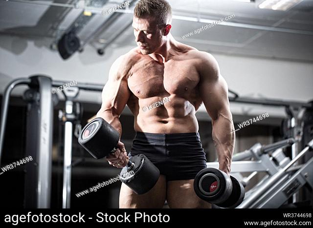 Bodybuilder in gym at fitness training with barbells standing in front of equipment