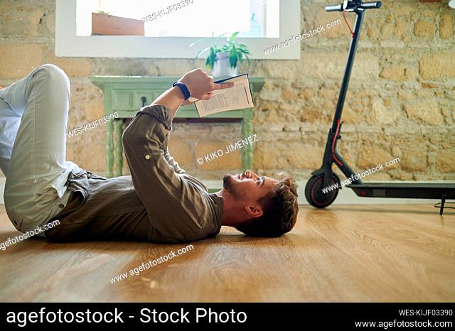 Caucasian man lying on floor while reading book in living room