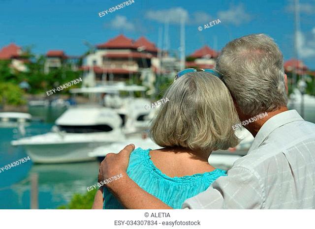 Happy cute senior couple on the pier with yachts