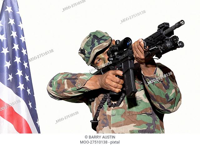 US Marine Corps soldier aiming M4 assault rifle with American flag against gray background