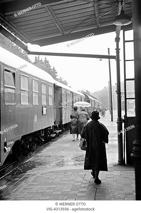 Sixties, black and white photo, people, senior, older woman walks on a platform to the waiting train, station, coat, hat, handbag, aged 60 to 70 years