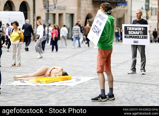31 July 2023, Bavaria, Nuremberg: An activist lays herself as a ""bloody steak"" on an oversized plate in front of the Lorenzkirche