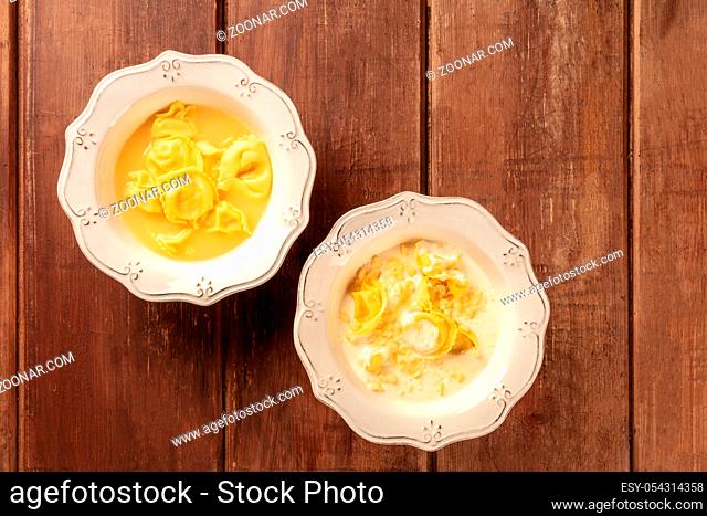 Tortellini served with broth and cream sauce, Italian food on a dark rustic wooden background with copy space