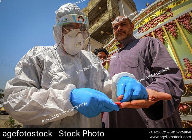 21 May 2020, Iraq, Baghdad: A health worker of the Ministry of Health wearing protective suit takes a blood sample from a man during a field examination to...