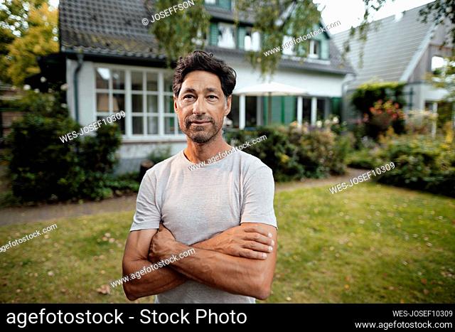 Mature man with arms crossed standing in front of house