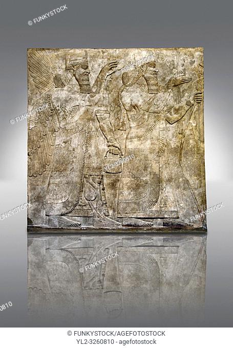 Assyrian relief sculpture panel of King Ashurnaspiral II, right, and a winged protective spirit holding a bucket of holy water in one hand and a cone in the...
