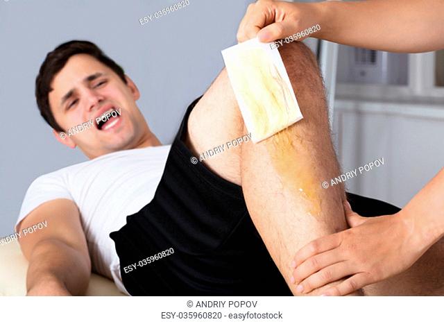 Man Screaming In Pain While Waxing Leg With Wax Strip