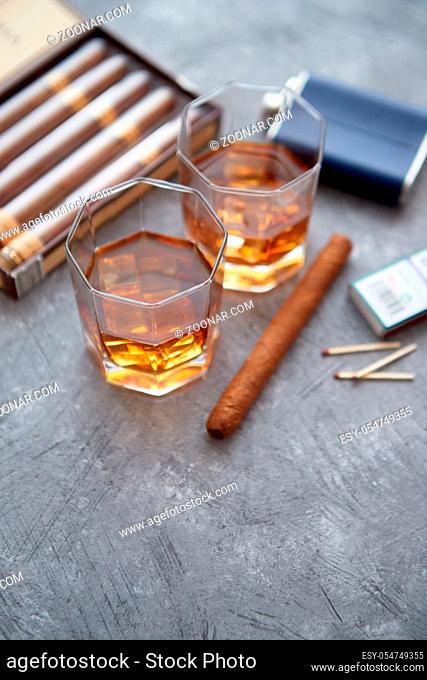 Carafe of Whiskey or brandy, glasses and box of finnest Cuban cigars on an gray stone table. With ice cubes