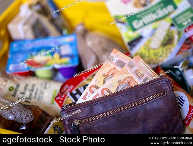ILLUSTRATION - 21 August 2023, Berlin: After shopping, a wallet filled with banknotes lies in a shopping basket filled with various groceries