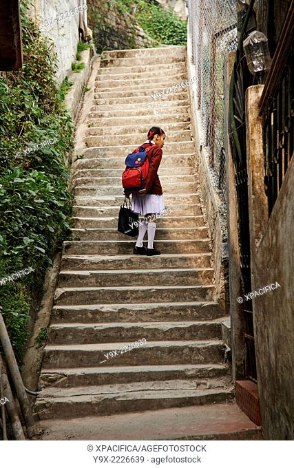 A young school girl walking up the stairs curious looks at something on the wall in the back streets of Darjeeling