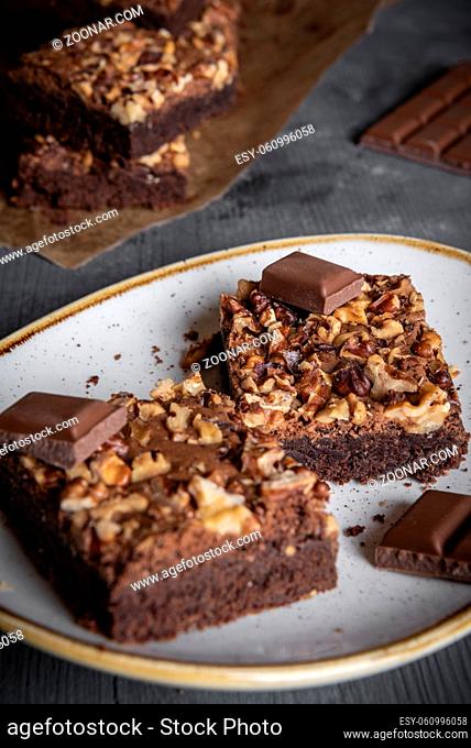 Portion of chocolate brownie cake and pieces of chocolate in a plate on a rustic wooden table. Chocolate cake with lots of walnuts on it