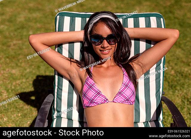 Mixed race woman wearing sunglasses sunbathing on sunbed in garden