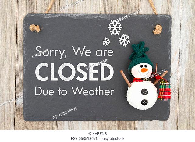 Closed due to weather sign, A chalkboard sign with a snowman with text Closed due to weather on weathered wood