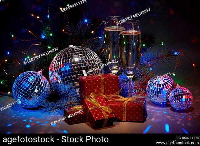 Champagne flutes, mirror balls (disco ball), fir branch, on dark background with colorful LED lights garland. New Year and Christmas