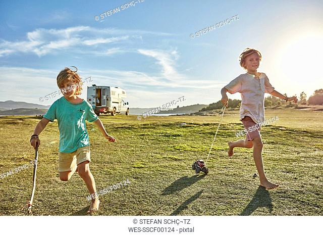Chile, Talca, Rio Maule, two boys running on meadow with toy cars beside camper