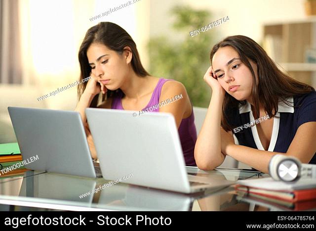 Two bored students waiting online content with laptops at home