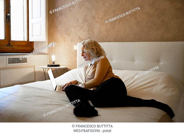 Mature businesswoman lying on bed working on laptop